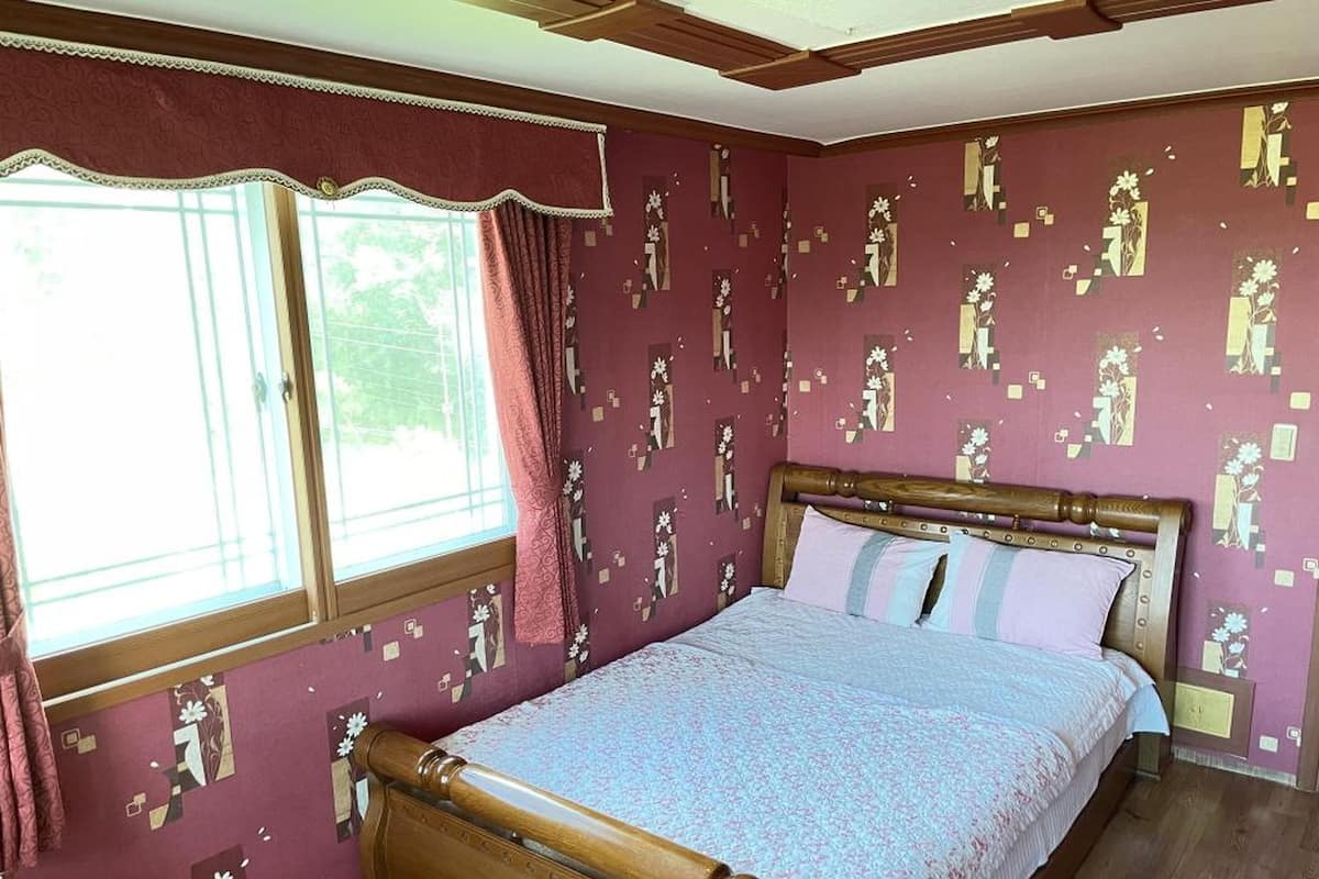 Un dormitorio con cama de madera, papel tapiz estampado y ventana con cortinas.