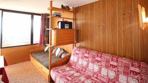 Une pièce avec un lit superposé, un canapé-lit, un mur en bois, une fenêtre et une petite table.