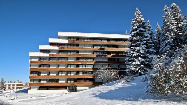 Un hôtel à plusieurs étages au design moderne, doté de balcons et offrant une vue sur un paysage enneigé.