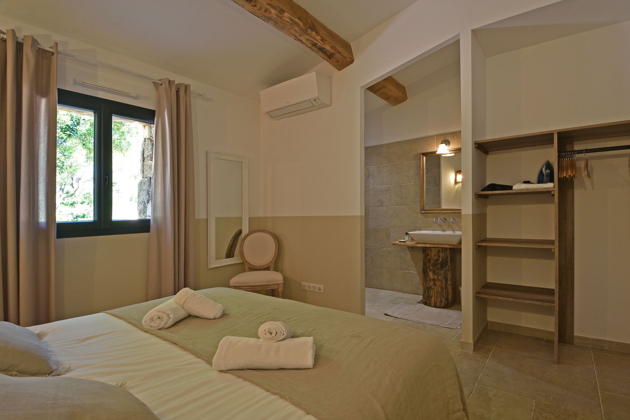 Una habitación de hotel con cama, baño con lavamanos y estante de madera.