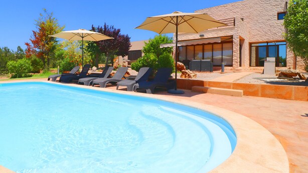 A swimming pool with lounge chairs and umbrellas, surrounded by a landscaped garden and a stone building. - Son Vigili 417 magnificent villa with private pool, jacuzzi, children's area and air-conditioning (Campos)
