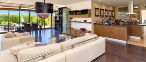 Een moderne woonkamer met een glazen salontafel, beige banken en een eethoek met een glazen tafel en stoelen.