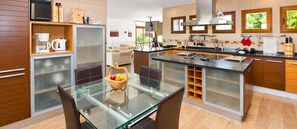 A modern kitchen with a glass dining table, wooden cabinets, and a central island with a sink.