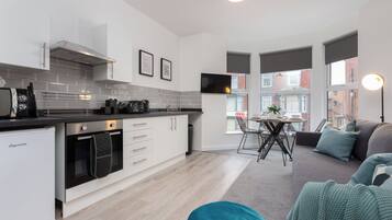 A modern kitchen with a built-in oven, a dining area with a table and chairs, and a sofa in the living room.