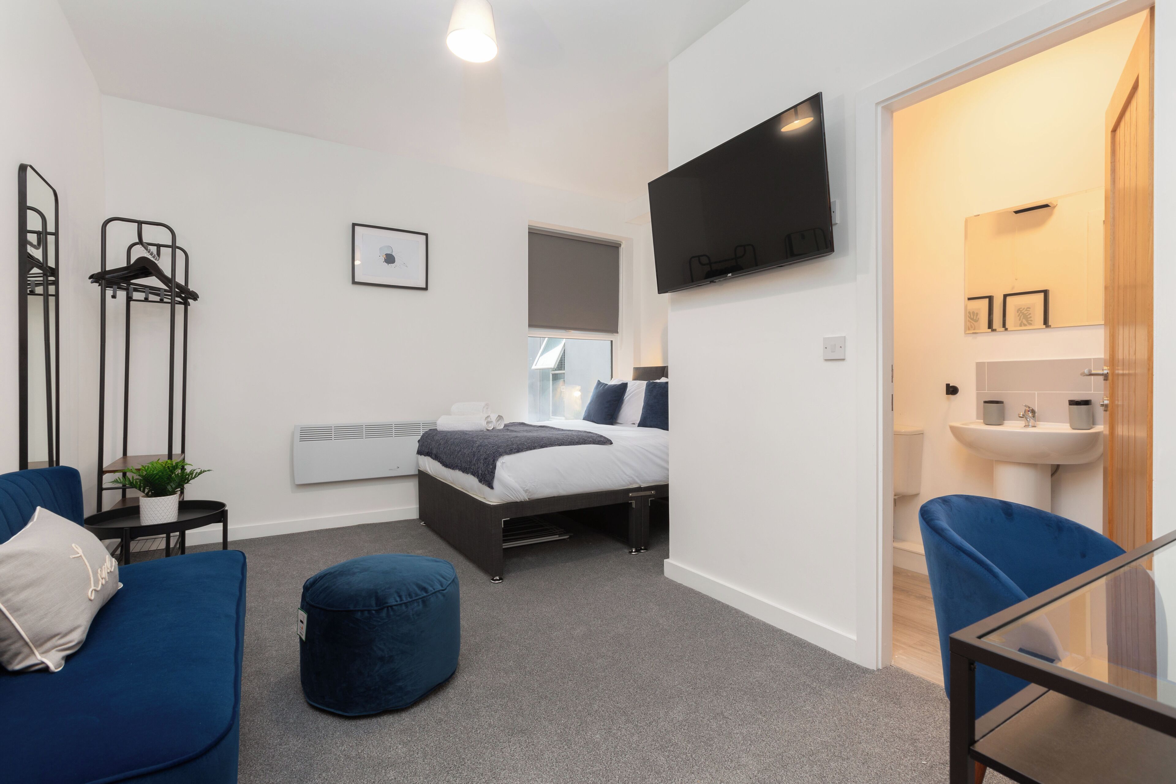 A modern bedroom with a bed, a TV, a desk, and a bathroom.