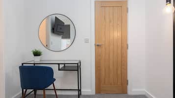 A room with a wooden door, a round mirror on the wall, a small table with a plant, and a blue chair.