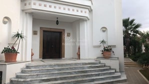 A white building with a dark wooden door, marble steps, and potted plants. - Prestigious villa in monastir (Monastir)
