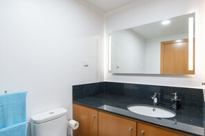 A bathroom with a white toilet, a sink with a black countertop, and a mirror above the sink. - Quiet and peaceful apartment with a private pool (Arco da Calheta)