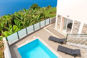 A rooftop pool with two lounge chairs, surrounded by lush greenery and a clear view of the ocean. - Quiet and peaceful apartment with a private pool (Arco da Calheta)