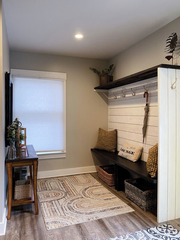 A room with a wooden bench, a wall-mounted coat rack, a basket, and a window with blinds. - West Side is the Best Side of Grand Rapids (Grand Rapids)