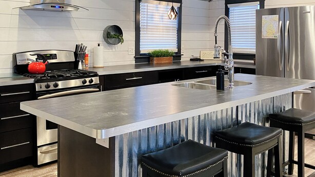 Une cuisine moderne dotée d’un grand îlot central, d’appareils électroménagers en acier inoxydable et de tabourets de bar noirs.