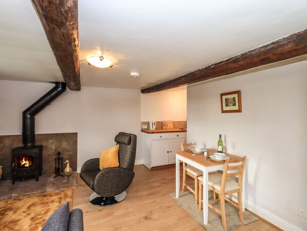 Una sala de estar acogedora con chimenea, un sillón cómodo, una mesa de comedor con sillas y una zona de cocina al fondo.