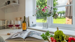 A kitchen counter with a cookbook, wine glasses, a bottle of wine, a vase with flowers, and fresh vegetables. - Holkham Skies, Wells-next-the-Sea, Norfolk (Wells-next-the-Sea)
