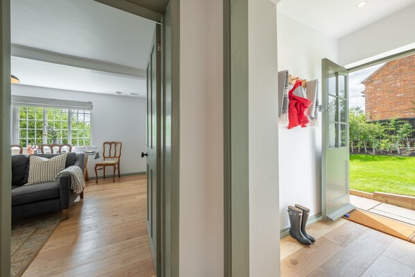 Un salon spacieux avec un canapé et des fauteuils, un coin repas et une vue sur un bâtiment en briques et un jardin, visible à travers une porte vitrée.