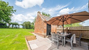 A patio with a table and chairs, a brick structure, and a wooden fence. - Holkham Skies, Wells-next-the-Sea, Norfolk (Wells-next-the-Sea)
