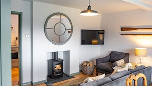 A living room with a fireplace, a sofa, a television, and a wall-mounted wooden bat. - Holkham Skies, Wells-next-the-Sea, Norfolk (Wells-next-the-Sea)
