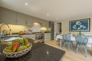 A modern kitchen with granite countertops, a dining area with blue chairs, and a painting on the wall.