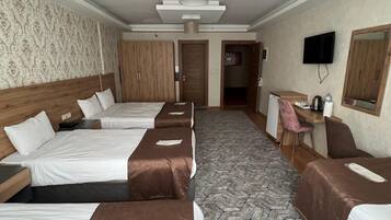 Hotellihuone, jossa on neljä sänkyä, työpöytä, tuoli, televisio ja kuviollinen matto.