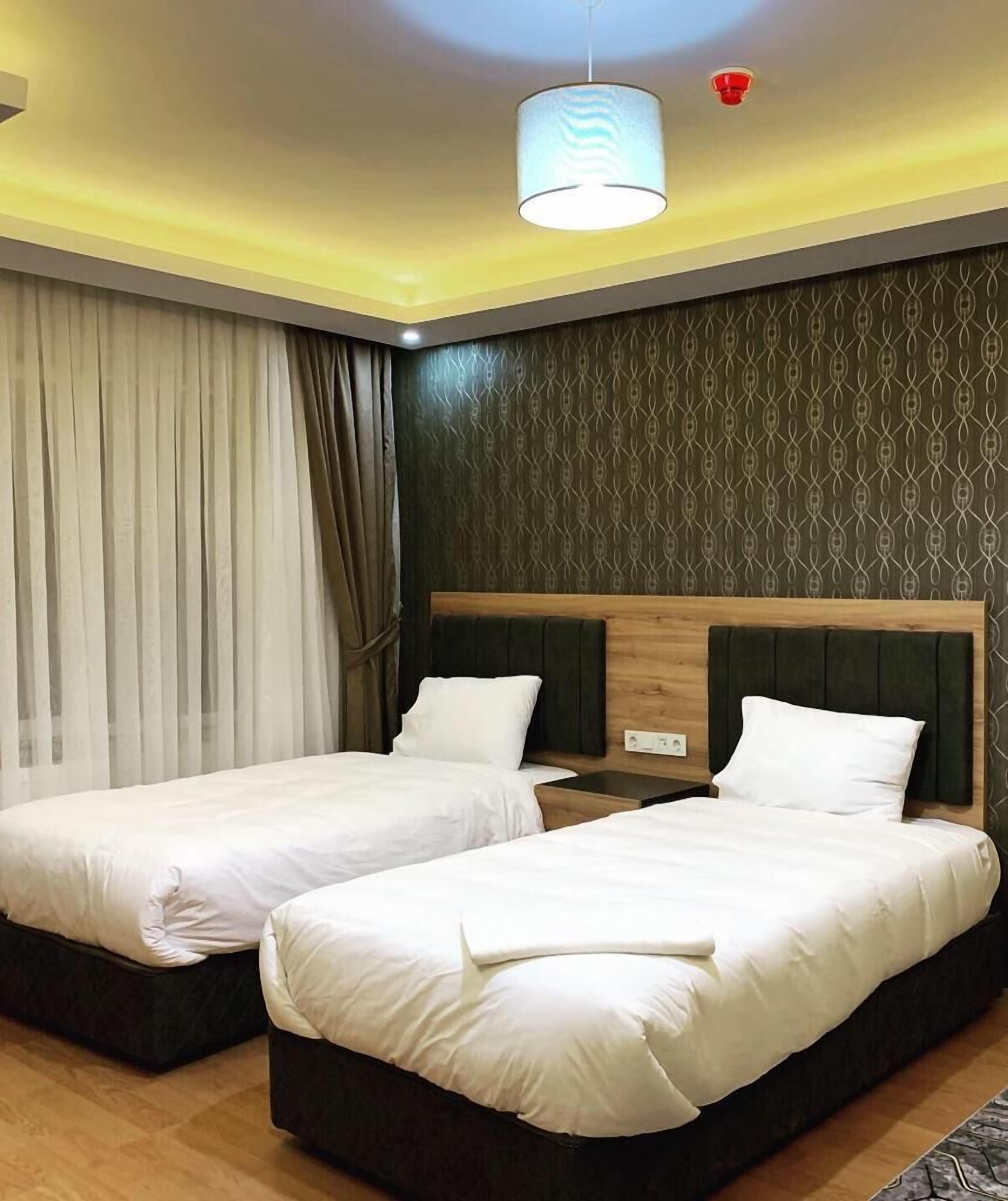 A hotel room with two beds, a patterned wall, a ceiling light, and a window with curtains.