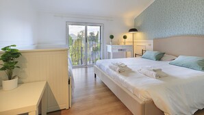 A bedroom with a large bed, a desk, a chair, and a balcony with a view of greenery. - Pandora Stresa (Stresa)