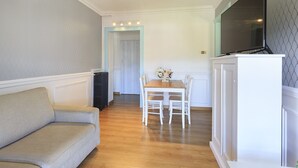 A compact living space with a sofa, a dining table with chairs, a flat-screen TV mounted on a cabinet, and a radiator. - Pandora Stresa (Stresa)