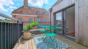 Una terraza de madera con un tapete estampado, muebles de jardín verdes y una planta en maceta.