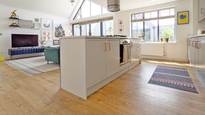 Una cocina moderna con horno integrado, una zona de comedor con sofá azul y un televisor sobre un mueble azul.
