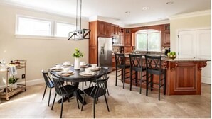 A modern kitchen with wooden cabinets, a central island with bar stools, a dining table with chairs, and a hanging light fixture. - Million Dollar View w/ 3 masters + Peloton on Pinehurst No. 9 (Pinehurst)