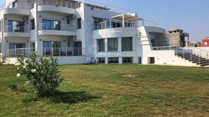 Un edificio residencial moderno de varios pisos, con balcones, una escalera central y un césped bien cuidado.
