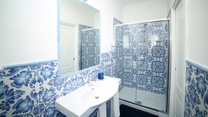 A bathroom with a white sink, a mirror, and a shower with blue floral tiles. - A Queen's room with Balcony (Sorrento)