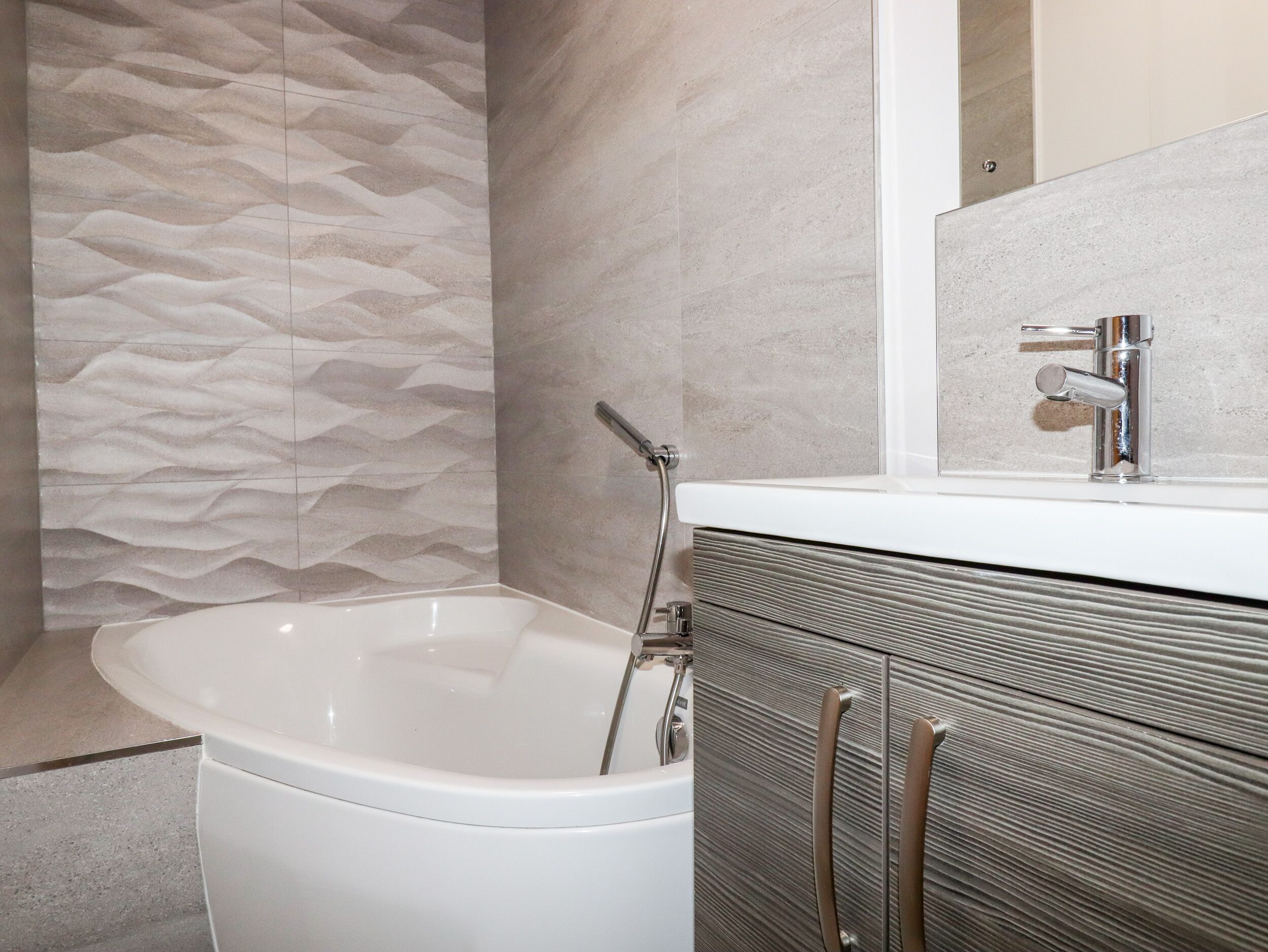 A modern bathroom with a freestanding bathtub, a built-in vanity with a mirror, and a textured wall.