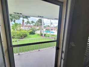 Een balkon met uitzicht op een aangelegde tuin, inclusief palmbomen en een zwembad.