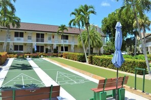 A courtyard with shuffleboard tables, benches, and palm trees.