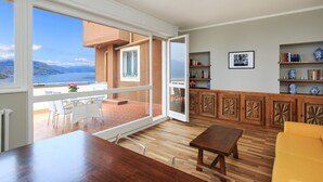 En rummelig opholdsstue med et træbord, en gul sofa og en balkon med havudsigt.