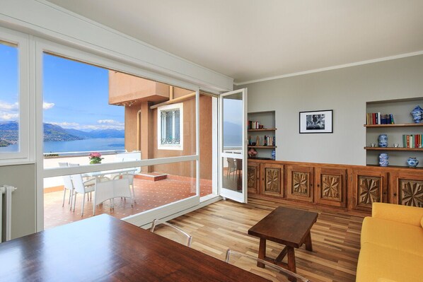 A spacious living area with a wooden dining table, a yellow sofa, and a view of the sea through large windows.