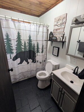 A bathroom with a shower curtain featuring a bear and trees, a toilet, a sink, and a mirror.