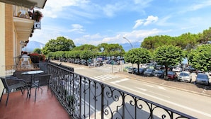 Un balcón con vista a una calle bordeada de coches aparcados y árboles.