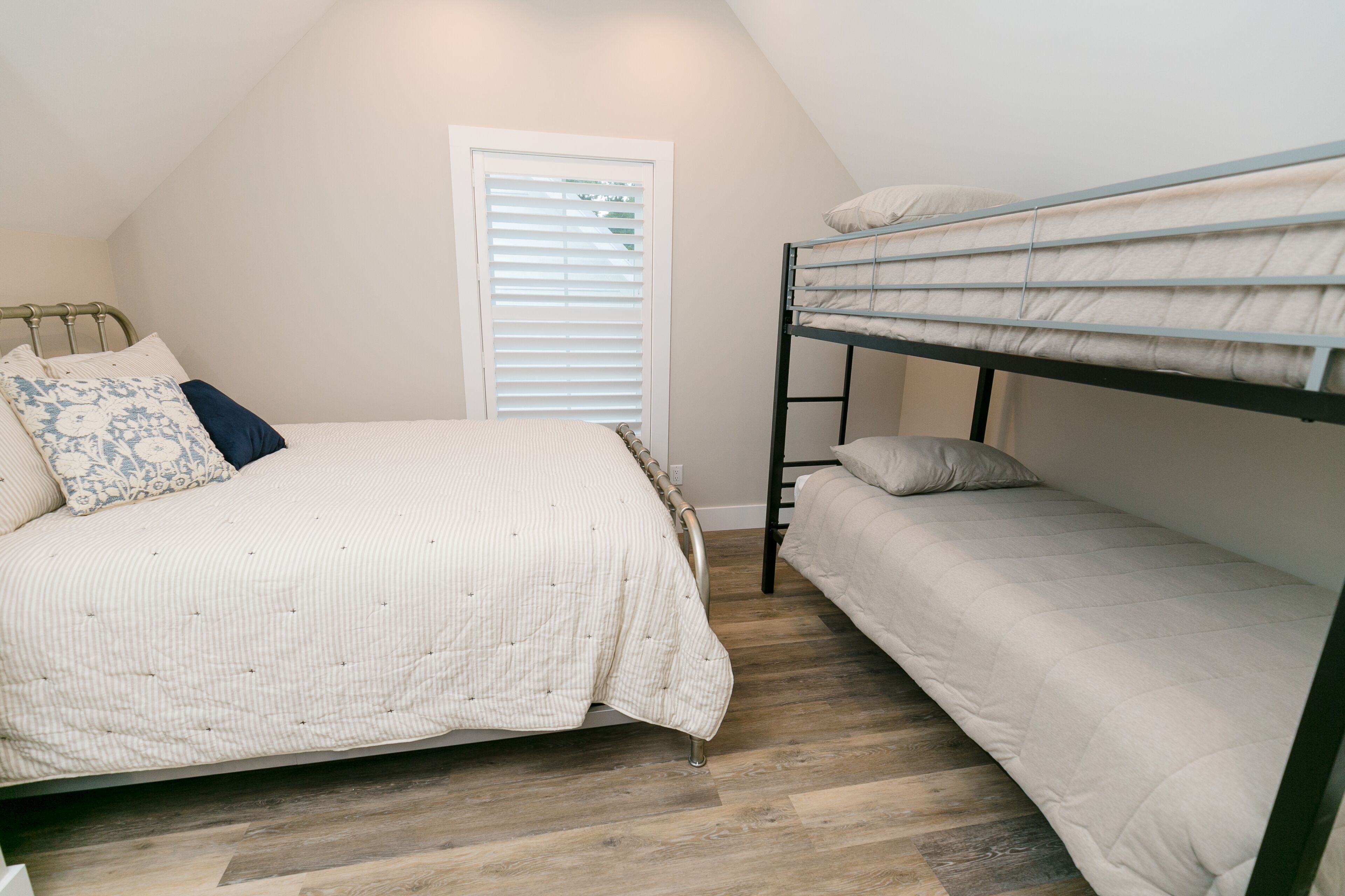 A bedroom with a bunk bed, a single bed, and a window with blinds.