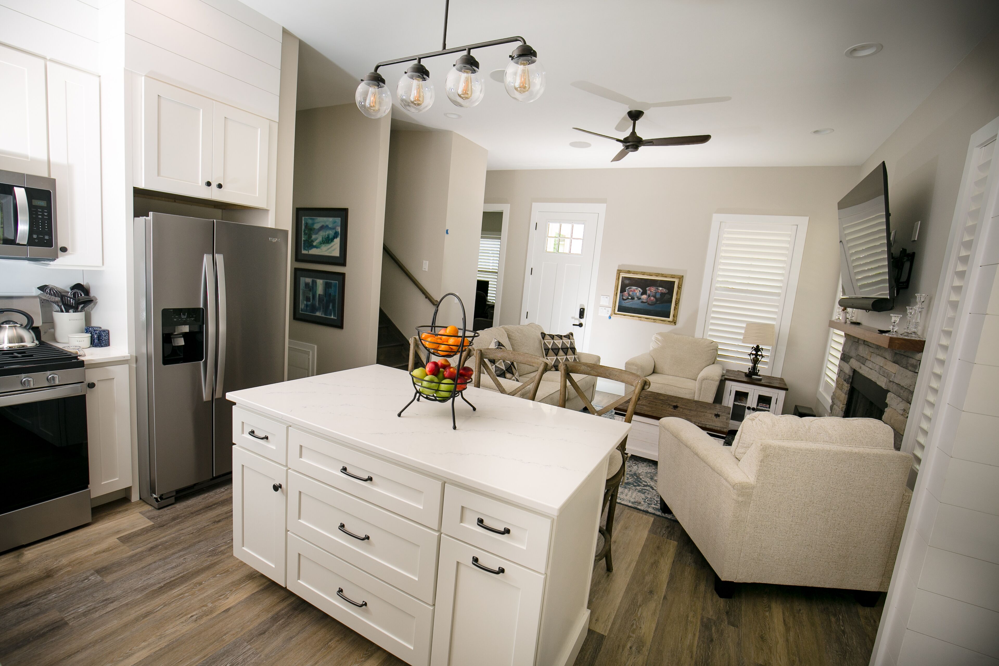 A modern kitchen with white cabinetry, a stainless steel refrigerator, and a fruit basket on the counter.