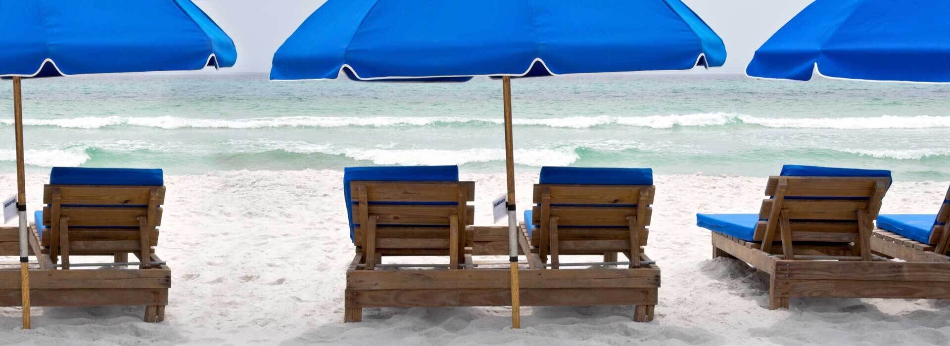 Una playa con sillones de madera y sombrillas azules.
