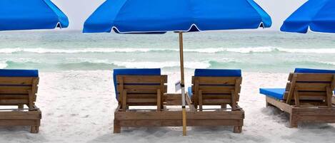 Una playa con sillones de madera y sombrillas azules.