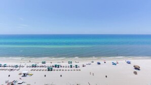 A beach with rows of sun loungers and umbrellas, a clear sky, and calm sea.