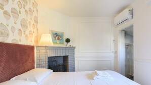 A hotel room with a bed, a fireplace, a wall with a hot air balloon wallpaper, and an air conditioning unit.