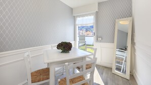 A dining area with a white table and chairs, a vase with flowers, and a view of the outside.