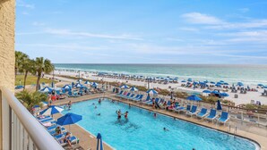 A swimming pool with lounge chairs and umbrellas, a beach with umbrellas and sun loungers, and a view of the ocean.