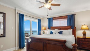 Un dormitorio con cama de madera, ventilador de techo, dos lámparas de noche, una ventana con cortinas y vistas al exterior.