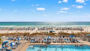 Una zona de piscina con sillones de playa y sombrillas, una playa con sombrillas y tumbonas, y vistas al océano.