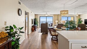A spacious living area with a large window, a ceiling fan, and a dining area with chairs and a table. - 2 Bedroom Deluxe Oceanfront with 2 Large Pool Facing Beautiful Beach (Panama City)