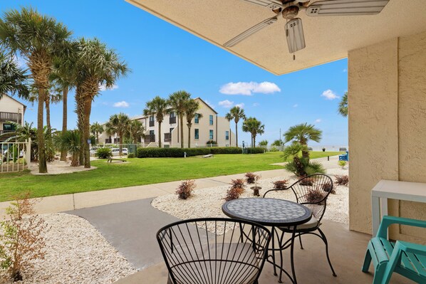 A patio area with outdoor seating, palm trees, and a building in the background.
