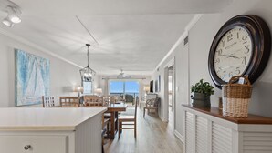 Una cocina amplia con una isla grande, un comedor con sillas, una lámpara colgante y un reloj en la pared.